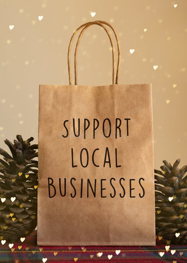 Sacchetto di carta di Natale di colore marrone con messaggio 'supporto alle imprese locali' davanti a uno sfondo beige con pinone