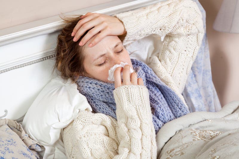 Sad alone young woman in white sweater and blue scarf feeling headache and cold sick and resting home in bed. holding her painful