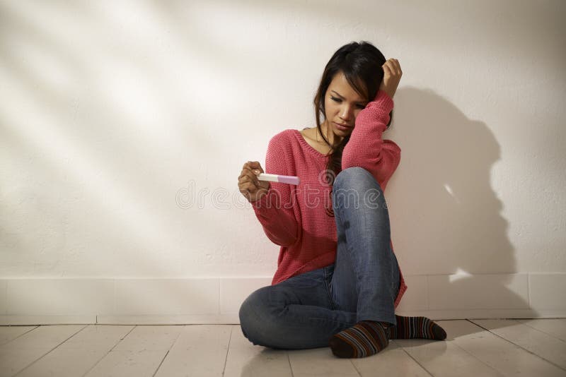 Sad Asian girl looking at pregnancy test sitting on floor