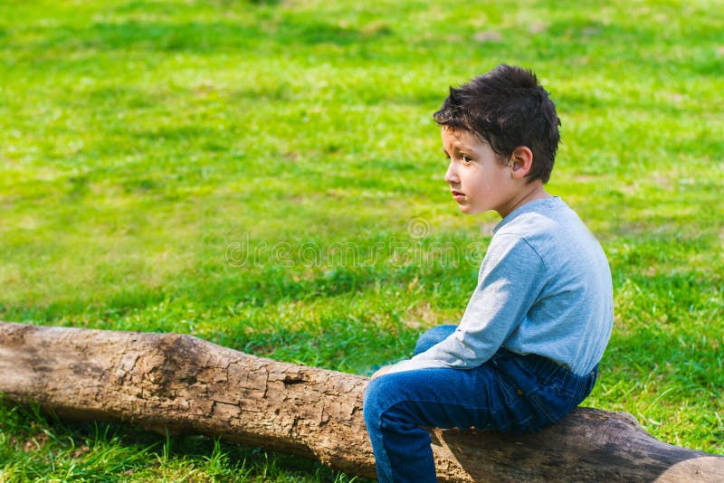 Boy 4 years old sitting alone on a log