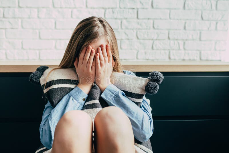 Sad Caucasian girl in depression hugs a pillow and closes her eyes with her hands on a background of a white brick wall. Thinks ab royalty free stock photography Sad Caucasian girl in depression hugs a pillow and closes her eyes with her hands on a background of a white brick wall. Thinks ab royalty free stock photography