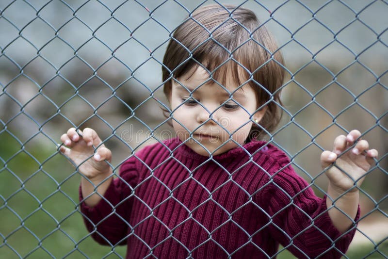 Sad child behind fence