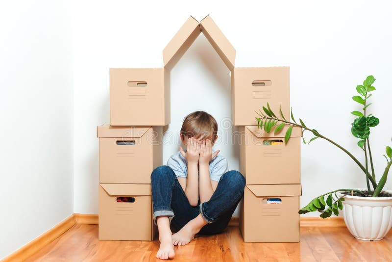 Sad child hiding in house making from boxes. Mortgage, people, housing, moving and real estate