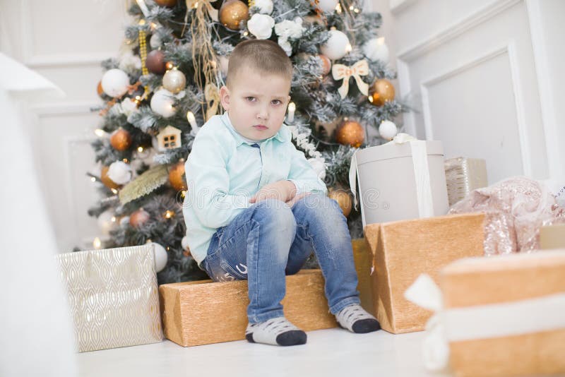 Sad child at the New Year tree. Upset little boy at christmas