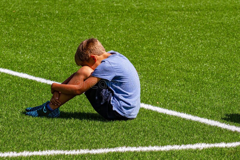 Sad disappointed boy sitting on the grass in stadium