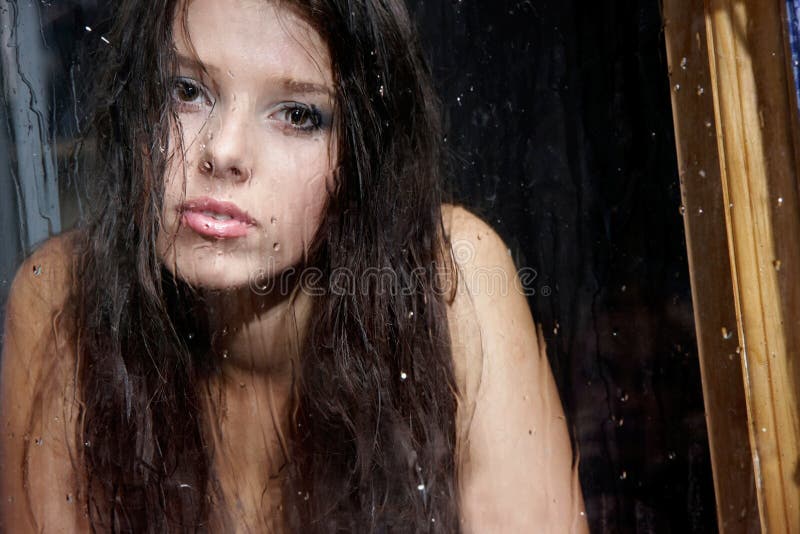 Sad girl behind wet window