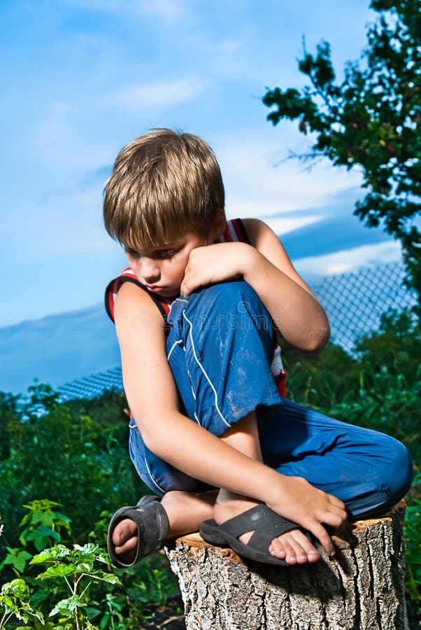 Sad little boy sitting on a stump