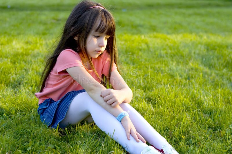 Smutné dievčatko sedí sám na trávnik.