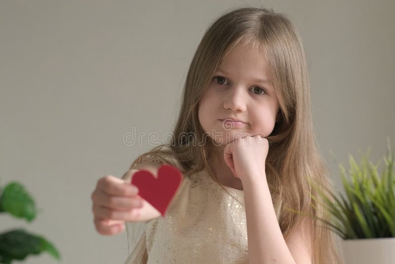 Sad little girl giving small handmade paper red heart for Valentines Day royalty free stock image