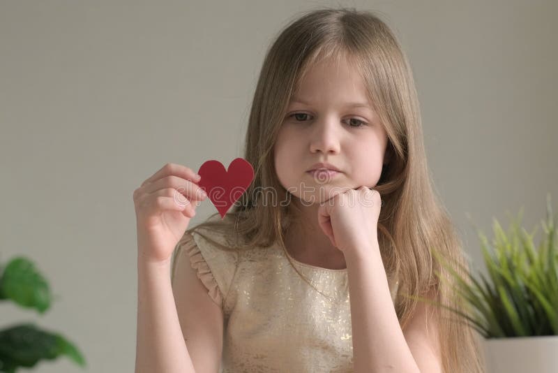 Sad little girl with small handmade paper red heart for Valentines Day royalty free stock photo