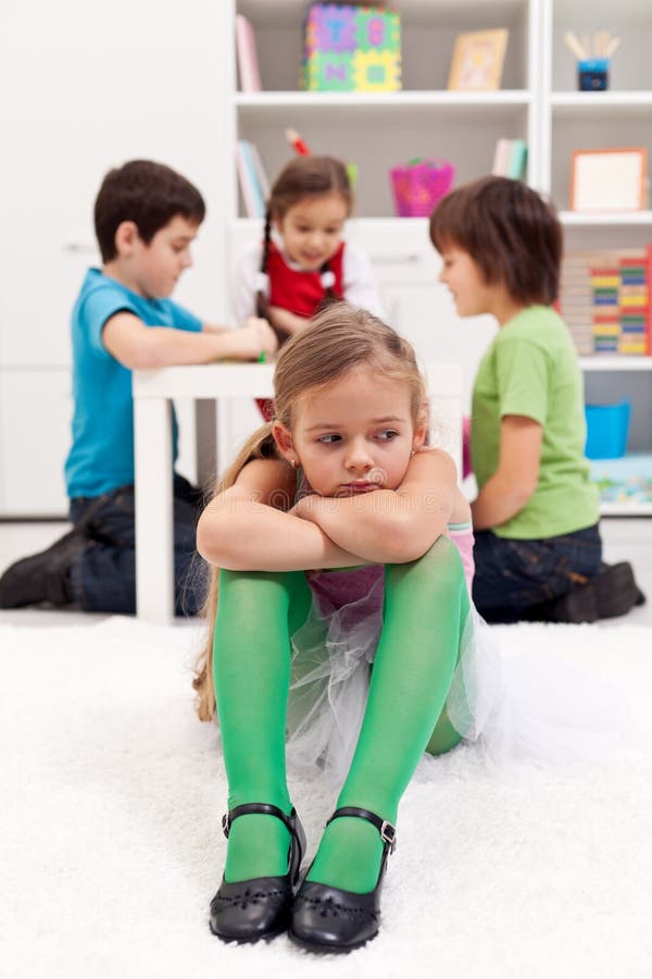 Sad little girl sitting excluded by friends