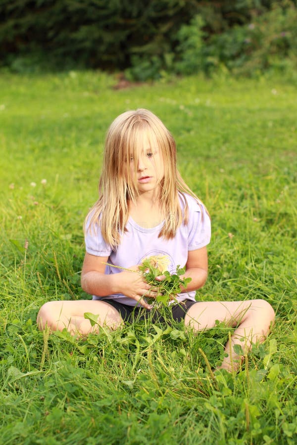Sad little girl in soft blue t-shirt and black shorts sitting on grass.