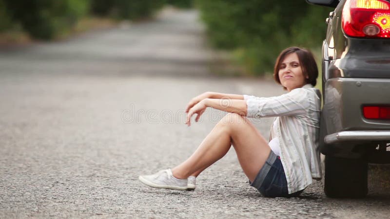 Sad pretty girl sitting on the road after car accident