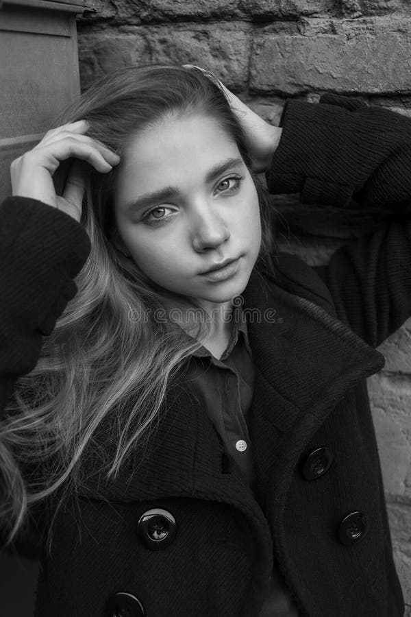 Sad sensual girl with long hair in black coat sitting near the wall. Concept of melancholy. Black and white image stock photos Sad sensual girl with long hair in black coat sitting near the wall. Concept of melancholy. Black and white image stock photos
