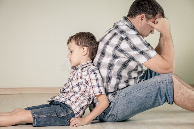 Sad son and his dad sitting on the floor at room at the day time stock imag...