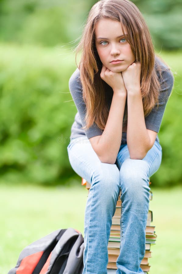 Sad student girl sitting on books