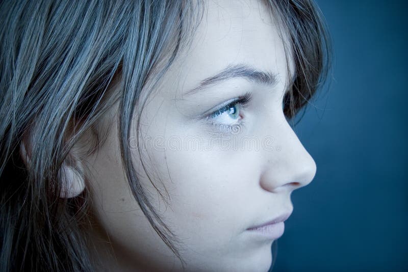 Closeup profile of a teen girl with sad expression, eyes looking upward. Blue tint. Isolated on blue background. Horizontal format. Closeup profile of a teen girl with sad expression, eyes looking upward. Blue tint. Isolated on blue background. Horizontal format.