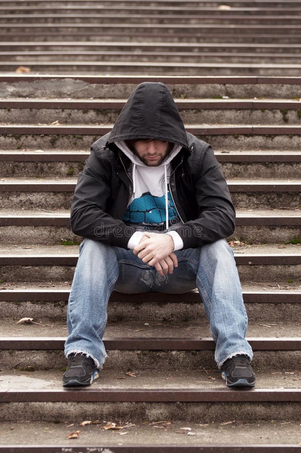 Sad teenage boy with hood sitting on stairs