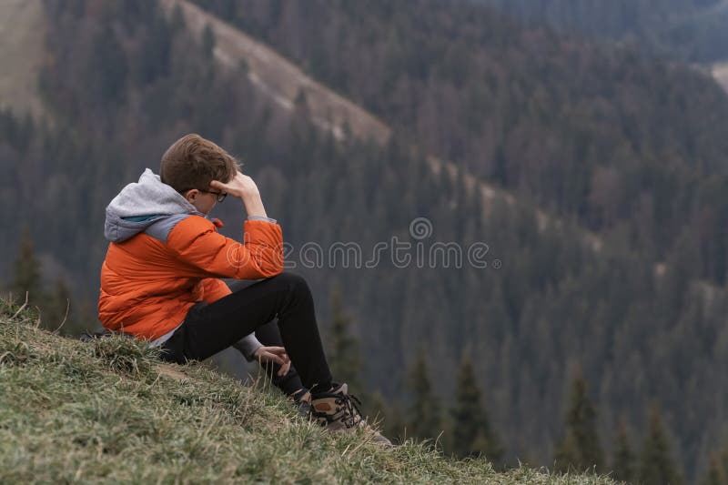 Sad teenager sits on hillside. Boy resting in mountains. Portrait of child in the autumn on hike