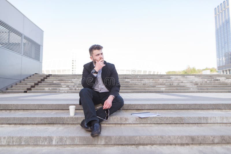 Sad, thoughtful business man sits on the steps and looks to the side
