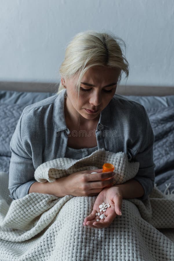 sad woman with climax sitting in bed and looking at bottle with painkillers,stock image