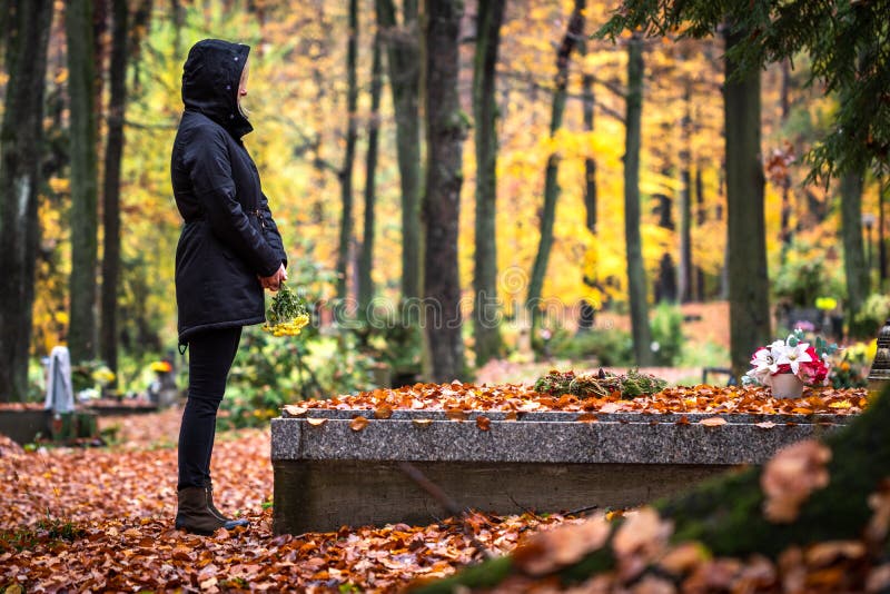 Sad woman is mourning for dead person at grave in cemetery