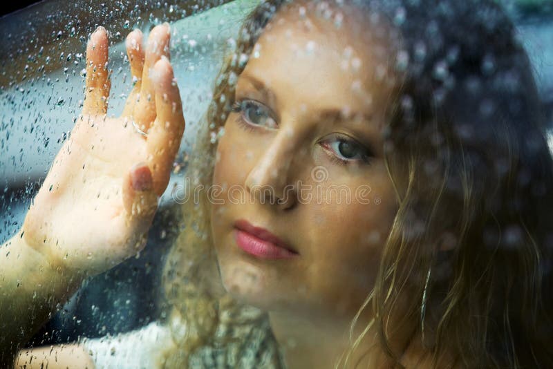 Smutný mladá žena při pohledu přes okno automobilu s kapkami deště.