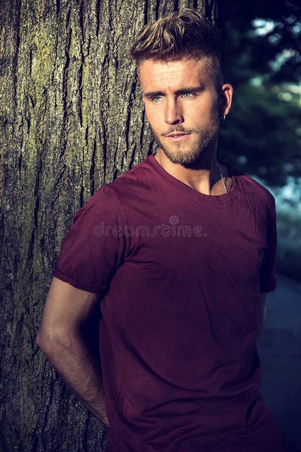 Sad, worried blond young man against tree stock photo Sad, worried blond young man against tree stock photo
