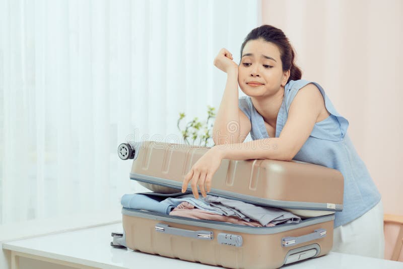 Sad young woman packing suitcase at home. Travel concept