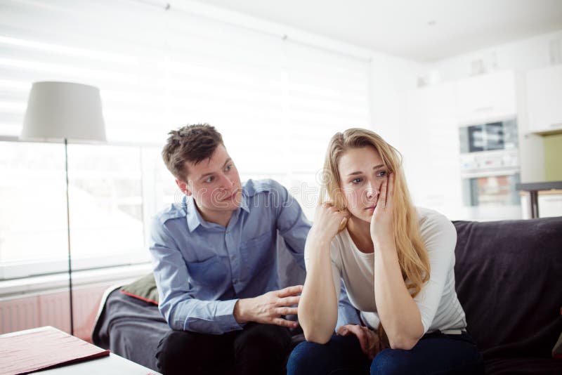 Sad young women sitting on the couch with her boyfriend. Couple arguing in their living room. Sad young women sitting on the couch with her boyfriend. Couple arguing in their living room.