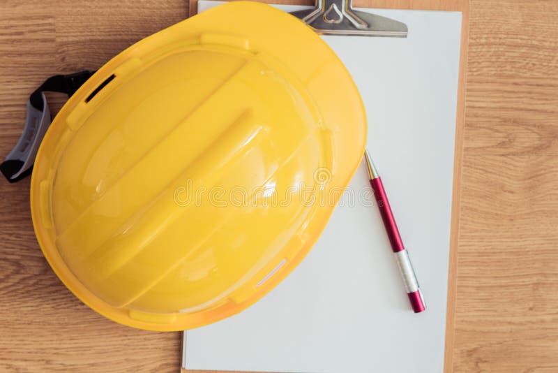 Safety helmet, clipboard, notebook, pen on wooden table