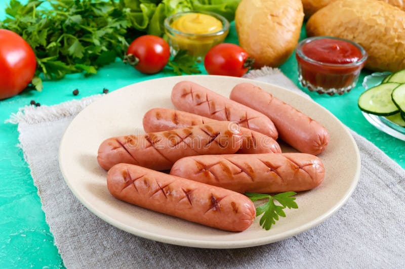 Saftiga grillade korvar, nya grönsaker, gräsplaner och frasiga bullar på en ljus bakgrund arkivbild Saftiga grillade korvar, nya grönsaker, gräsplaner och frasiga bullar på en ljus bakgrund arkivbild