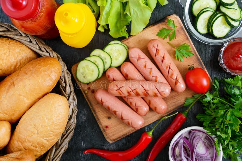 Saftiga grillade korvar, såser, nya grönsaker, frasiga bullar, på en träbakgrund royaltyfri bild Saftiga grillade korvar, såser, nya grönsaker, frasiga bullar, på en träbakgrund royaltyfri bild