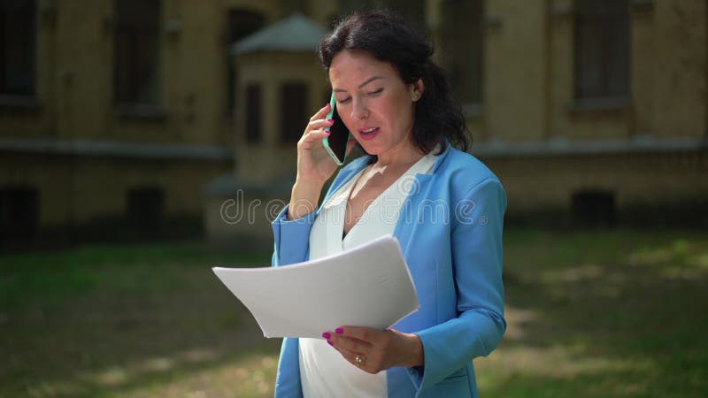 Saggia e bella imprenditrice incinta che parla al telefono, analizza le scartoffie all'aperto al sole. ritratto di