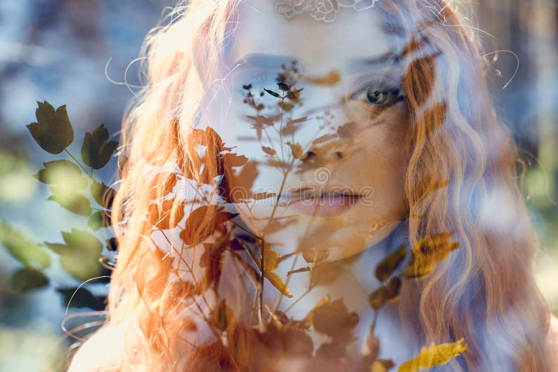 Fabulous portrait of a red-haired girl in nature with double exposure and glare. Beautiful redhead girl with long hair in the forest, mysterious look and big eyes, leaves and grass on her face. Fabulous portrait of a red-haired girl in nature with double exposure and glare. Beautiful redhead girl with long hair in the forest, mysterious look and big eyes, leaves and grass on her face