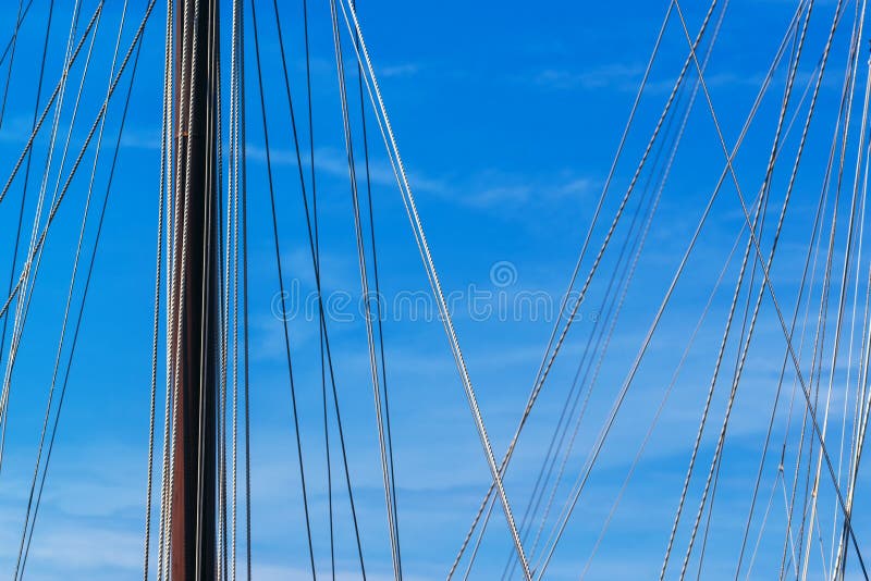 Sailboat mast and ropes in harbor against blue sky