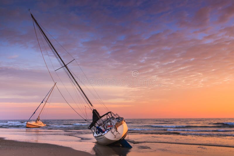 Two sailboats beached on the sand of Cape Hatteras National Seashore Pea Island in North Carolina at sunrise. Two sailboats beached on the sand of Cape Hatteras National Seashore Pea Island in North Carolina at sunrise.