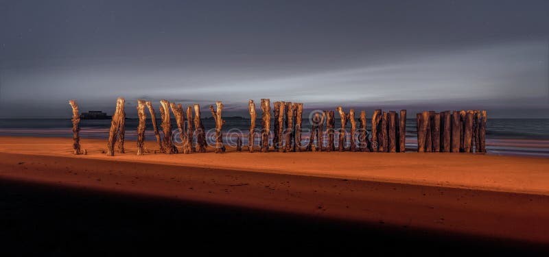 Saint Malo beach wooden pillars lit by the street lamps during the sunset