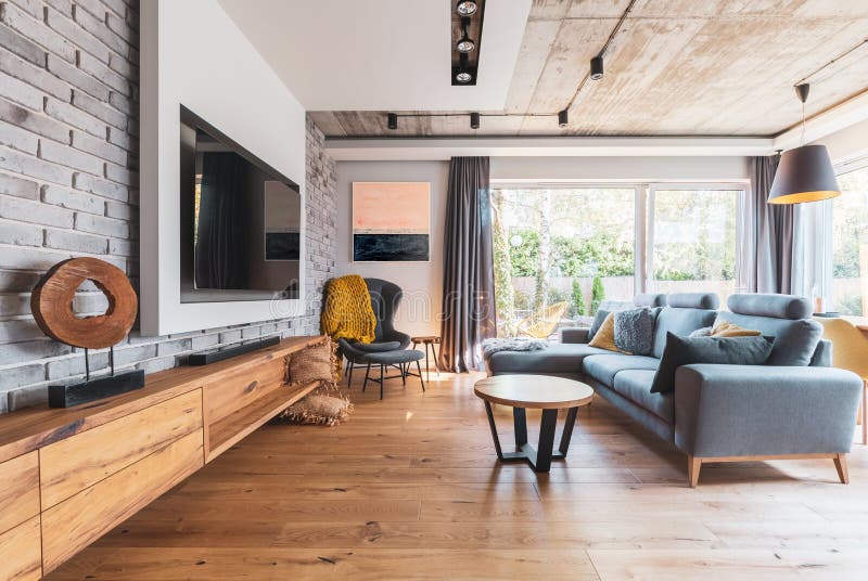 sala de estar com chão leve de madeira, sofá cinza e cadeira traseira de asa e tv grande na parede