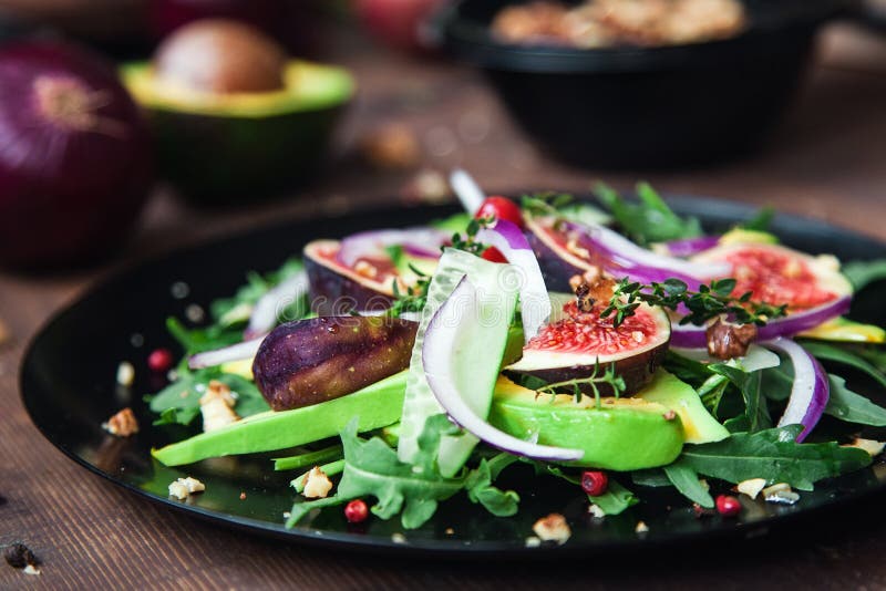 Salad on a black plate: arugula, figs, avocado, red onions, cucumbers, walnuts, viburnum, thyme, spices stock photography Salad on a black plate: arugula, figs, avocado, red onions, cucumbers, walnuts, viburnum, thyme, spices stock photography