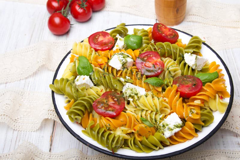 Salad with colorful pasta, cherry tomatoes, feta cheese and fresh basil