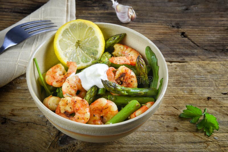 salad from prawn shrimp, green asparagus, arugula, garlic, parsley and lemon slice in a bowl on a rustic wooden table with copy s