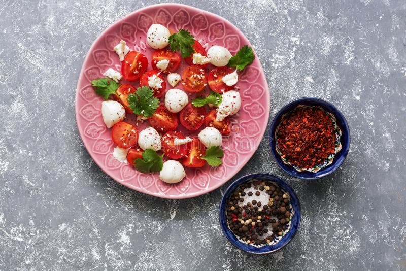 Salada de Caprese, tomates de cereja, mussarela e verdes em uma placa cor-de-rosa em um fundo cinzento Alimento italiano Vista su imagens de stock royalty free Salada de Caprese, tomates de cereja, mussarela e verdes em uma placa cor-de-rosa em um fundo cinzento Alimento italiano Vista su imagens de stock royalty free