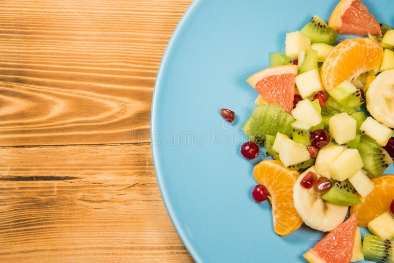 Salada de fruto fresco com citrino em uma placa azul que esteja em uma tabela de madeira com um lugar para a inscrição imagem de stock royalty free Salada de fruto fresco com citrino em uma placa azul que esteja em uma tabela de madeira com um lugar para a inscrição imagem de stock royalty free