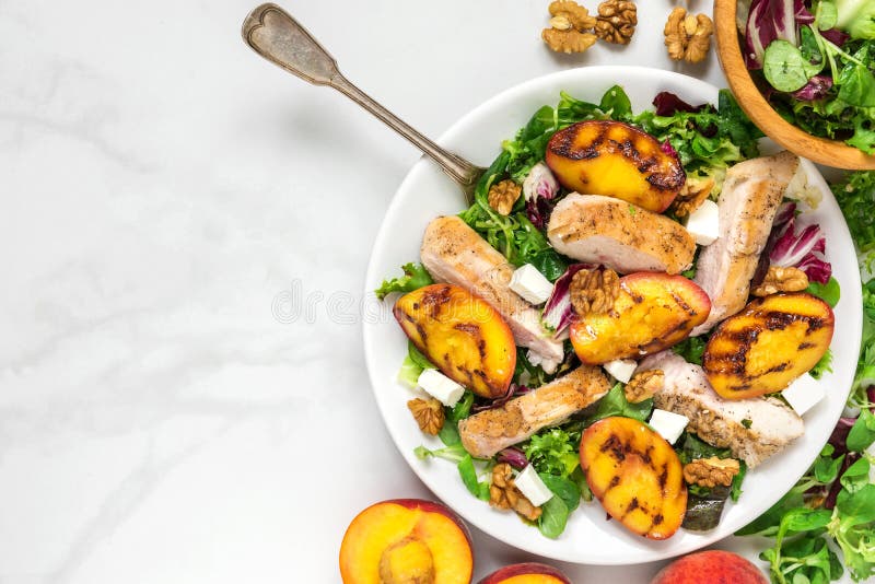 Salade de poulet avec la pêche grillée, salade mixte, feta et noix dans un plat avec la fourchette Nourriture saine dessus photo stock Salade de poulet avec la pêche grillée, salade mixte, feta et noix dans un plat avec la fourchette Nourriture saine dessus photo stock