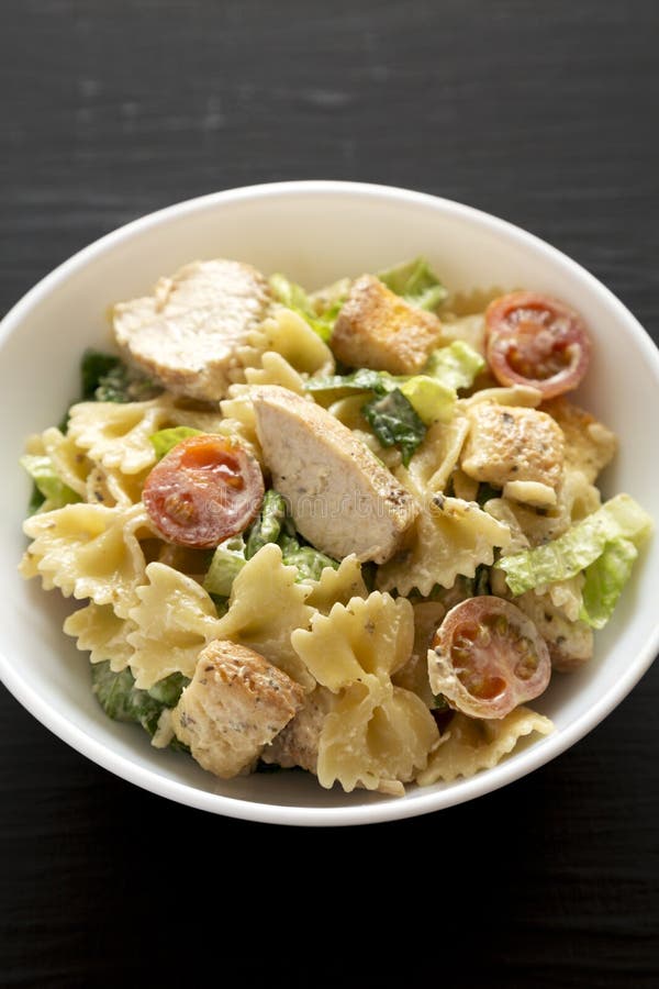 Salade de pâtes maison de César de poulet dans un bol blanche sur une vue latérale sur fond noir. Gros plan photo libre de droits