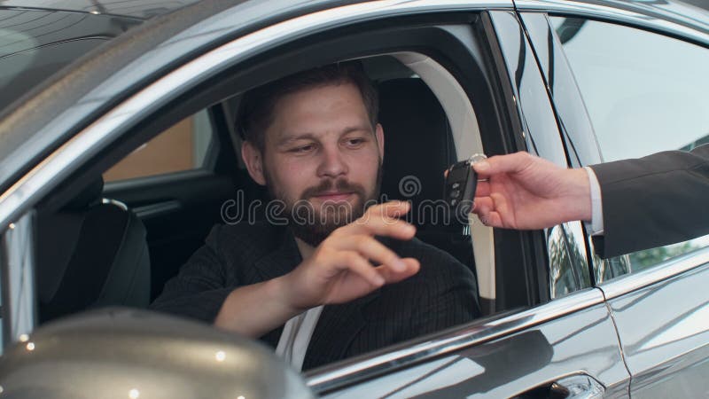 Sales manager handing over the keys to man that sitting in the car.