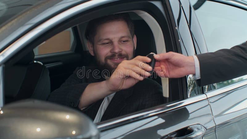 Sales manager handing over the keys to man that sitting in the car.