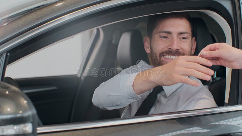 Sales manager handing over the keys to man that sitting in the car.