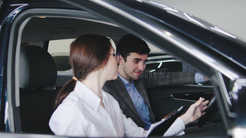 Sales Professional parla delle opzioni dei veicoli con i clienti all'interno di moderni concessionari di auto nelle ore pomeridian video d archivio